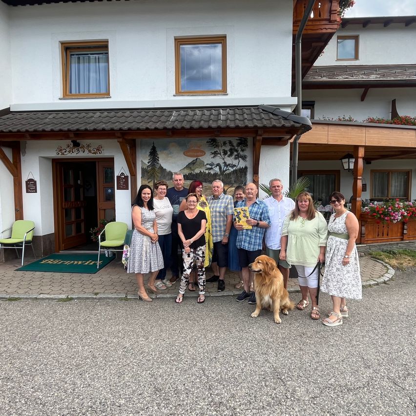 Eine Gruppe von Menschen, einschließlich Erwachsener und eines Hundes, posiert für ein Foto vor einem Gebäude mit einem Wandbild.