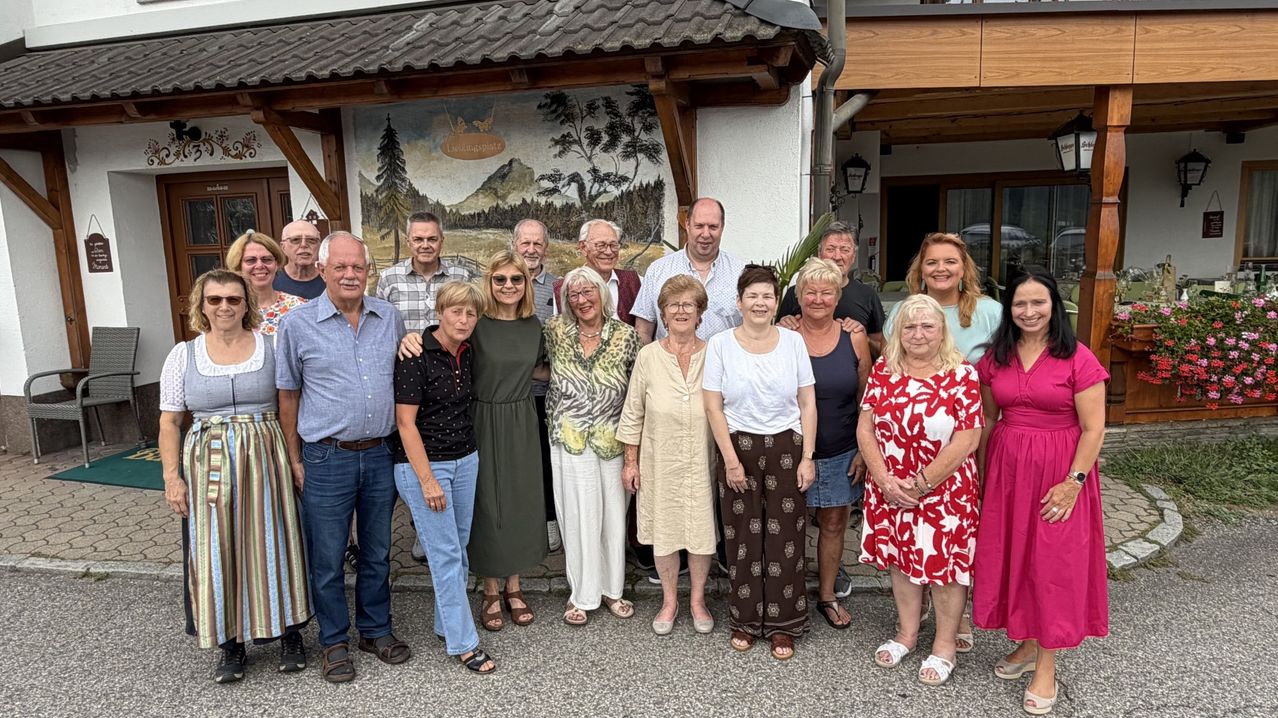 Eine Gruppe von Menschen, möglicherweise eine Familie, posiert für ein Foto vor einem Gebäude mit einem Wandbild.