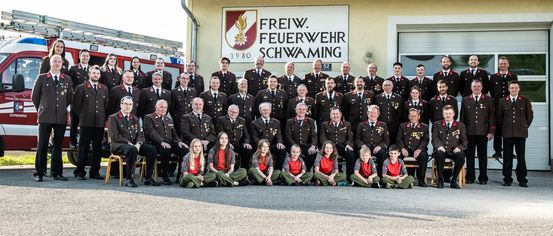 Ein Gruppenfoto von Freiw. Feuerwehr Schwaming-Mitgliedern, mit Feuerwehrleuten und jungen Mädchen in Uniformen, die vor einem Gebäude stehen und sitzen.