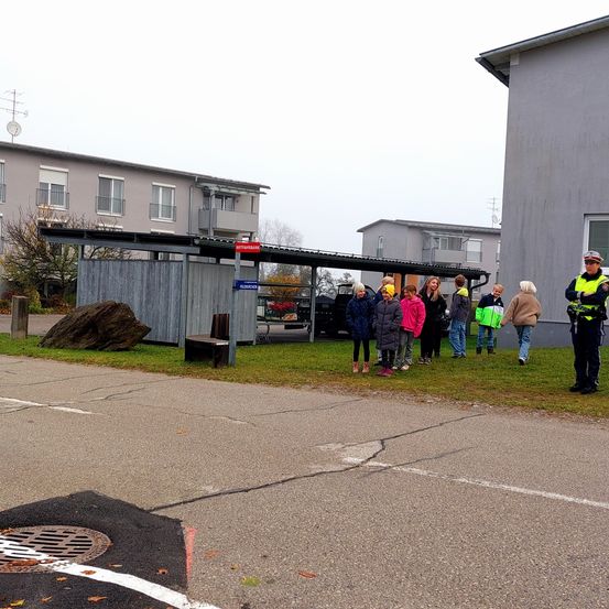 Eine Gruppe von Kindern und Erwachsenen steht vor einem Gebäude mit einem Polizisten. Die Kinder tragen Winterkleidung.
