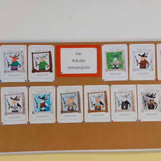 Ein Bulletinboard zeigt mehrere Illustrationen von Charakteren, die als Räuber gekleidet sind, jeweils mit einem Namensschild versehen. Oben am Board befindet sich ein Schild auf Deutsch mit der Aufschrift 'Der Räuber Hotzenplotz'.