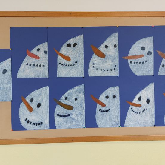 Ein Bulletinbrett mit neun Schneemannzeichnungen in einem Rastermuster. Jeder Schneemann hat ein blaues Gesicht und eine rote Nase. Das Brett ist auf einem braunen Holzrahmen montiert.