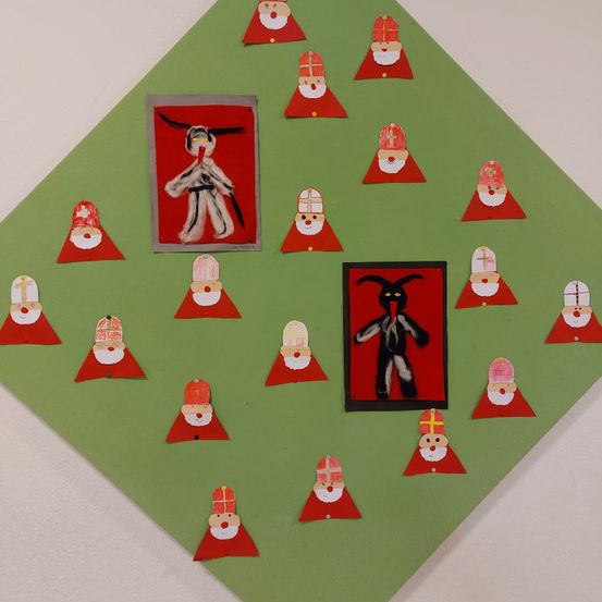 Eine grüne rautenförmige Anzeige zeigt mehrere Weihnachtsmannfiguren mit roten Mützen und Bärten. In der Mitte befinden sich zwei gerahmte Bilder; eines zeigt eine Figur mit langem Bart und Horn, das andere einen Weihnachtsmann in Kampfsportkleidung.