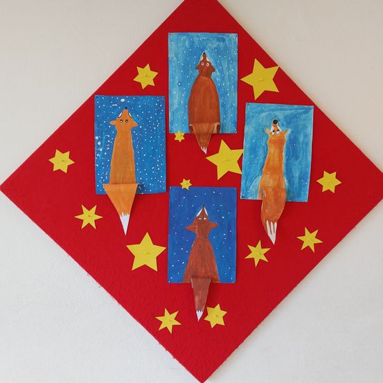 Ein rotes rautenförmiges Kunstwerk zeigt vier Fuchsgemälde, jedes auf blauem Hintergrund. Die Füchse sind von gelben Sternen umgeben. Das Stück ist an einer weißen Wand befestigt.
