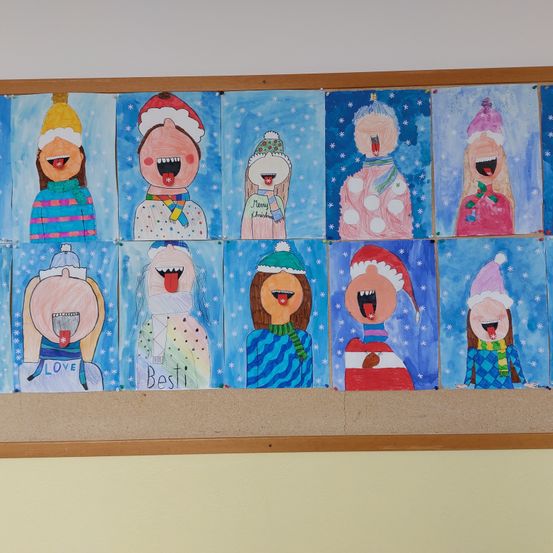 Ein Bulletin-Board zeigt verschiedene farbenfrohe winterliche Zeichnungen. Jede Zeichnung zeigt eine Figur in Winterkleidung wie Mützen und Schals, wobei die Zungen herausgestreckt sind. Einige Figuren haben 'LIEBE' und 'Besti' darauf geschrieben.
