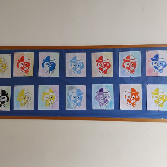 Ein Bulletinboard zeigt mehrere farbenfrohe Clowngesichtsgemälde, jedes mit Hut und Fliege. Die Gemälde sind in verschiedenen Farben und Schattierungen, angeordnet in einem Raster auf einem blauen Hintergrund.