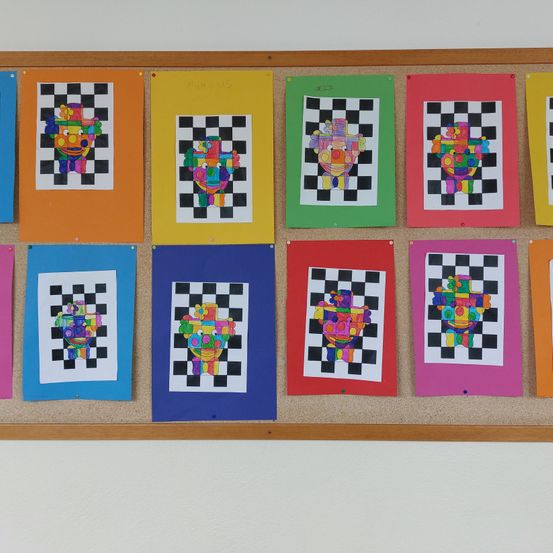 Ein Pinnwand mit farbenfrohen Bildern von Clown-Gesichtern in Schachbrettmuster. Jedes Bild ist auf einem quadratischen Papier angeheftet.