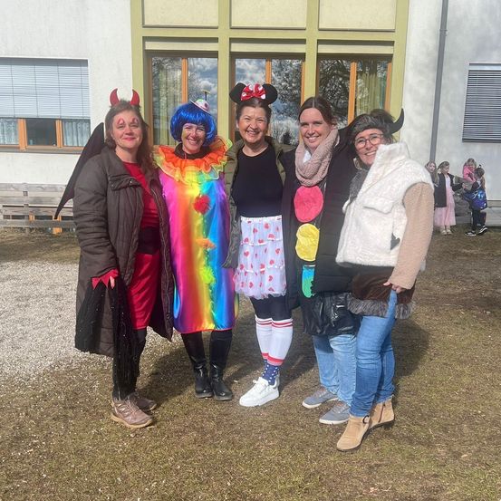 Fünf Frauen in Verkleidungen stehen vor einem Gebäude. Eine ist als Teufel verkleidet, eine andere als Clown und andere als Minnie Mouse und eine Jacke mit Fellfutter.