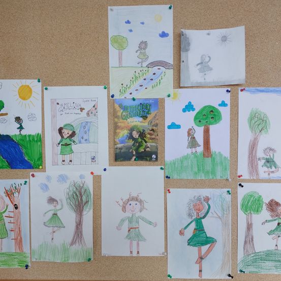 Ein Korkbrett zeigt verschiedene Kinderzeichnungen, darunter eine Sonne, Bäume und Figuren in grünen Kleidern. Einige Zeichnungen haben Text, andere sind abstrakter.