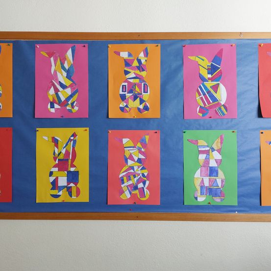 Ein Anschlagbrett mit acht farbenfrohen geometrischen Hasenausschnitten. Der Hintergrund ist blau und die Ausschnitte sind auf verschiedenfarbigem Papier.