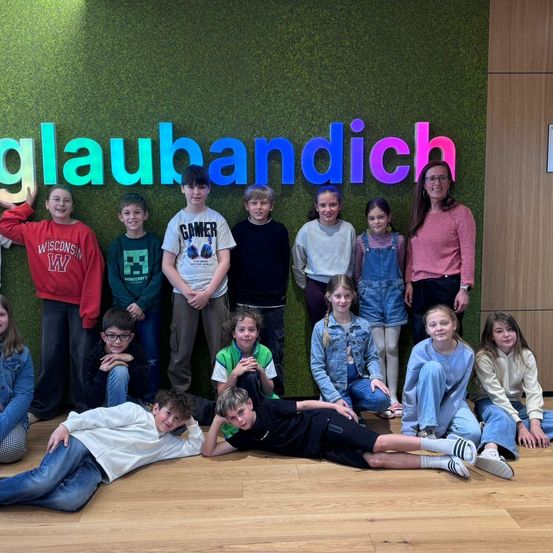 Eine Gruppe von Kindern und Erwachsenen posiert für ein Foto vor einer grünen Wand mit dem Wort glauberbandich.