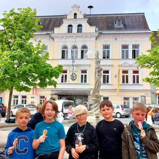 Fünf Jungen posieren für ein Foto vor einem Gebäude mit einem Brunnen. Ein Junge hält einen Eislutscher.