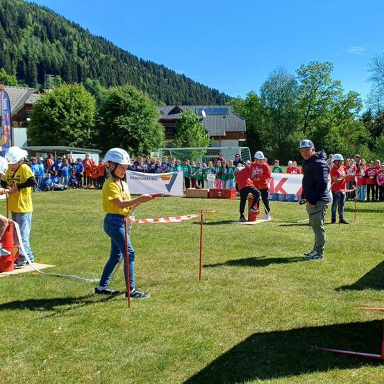 Eine Gruppe von Menschen in gelben Shirts nimmt an einer Veranstaltung auf einem Rasenfeld mit Bergen im Hintergrund teil. Mehrere Personen tragen Helme.