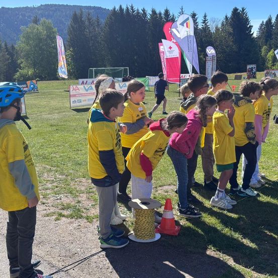 Eine Gruppe von Kindern in gelben Shirts steht auf Gras mit einem Fußballtor und Bannern im Hintergrund.