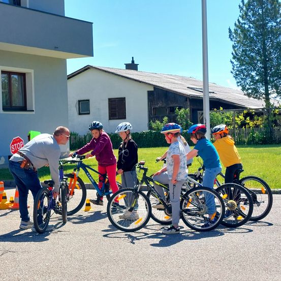 Eine Gruppe von Kindern mit Helmen lernt, ihre Fahrräder mit einem Mann vor ihnen an einem sonnigen Tag zu fahren.