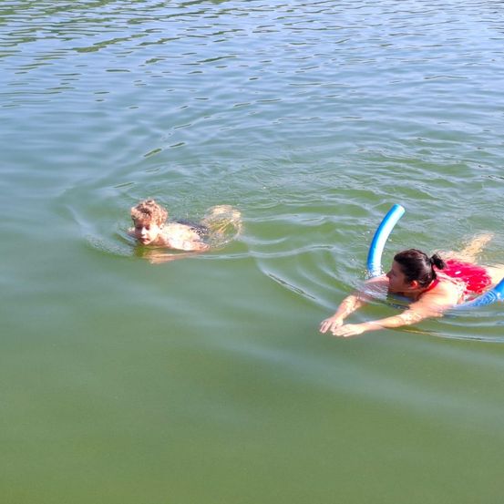 Ein kleiner Junge und eine Frau schwimmen im Wasser, beide halten blaue Schwimmhilfen.
