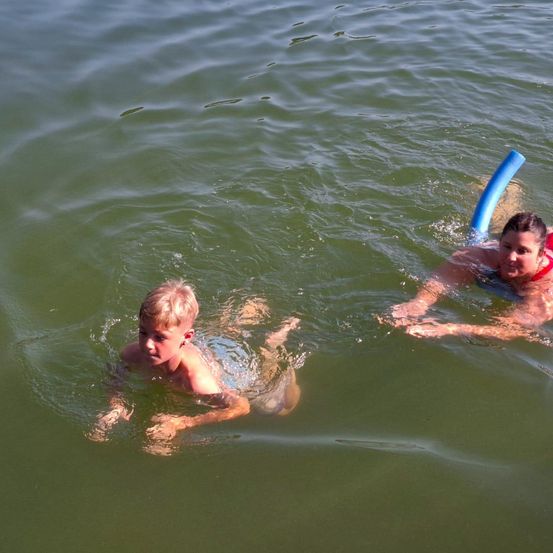 Ein Junge und eine Frau schwimmen im klaren Wasser. Der Junge trägt keine Schwimmhilfe. Die Frau trägt einen roten Schwimmweste.
