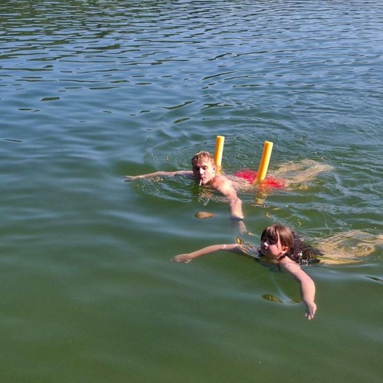 Zwei Kinder schwimmen mit Schnorchelausruestung im Wasser. Ein Junge raucht eine Zigarette.