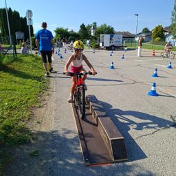 Ein Kind fährt auf einem Hügel auf einem Fahrrad, während andere in der Nähe Fahrradfähigkeiten üben.