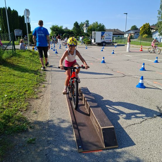 Ein Kind fährt auf einem Hügel auf einem Fahrrad, während andere in der Nähe Fahrradfähigkeiten üben.