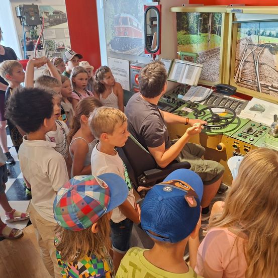 Eine Gruppe von Kindern beobachtet einen Mann, der einen Zugsimulator in einem Museum bedient.