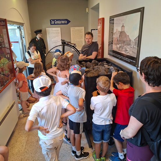 Eine Gruppe von Kindern und Erwachsenen ist in einem Museum und betrachtet eine Ausstellung von Steinen, während ein Mann in Polizeiuniform erklärt.