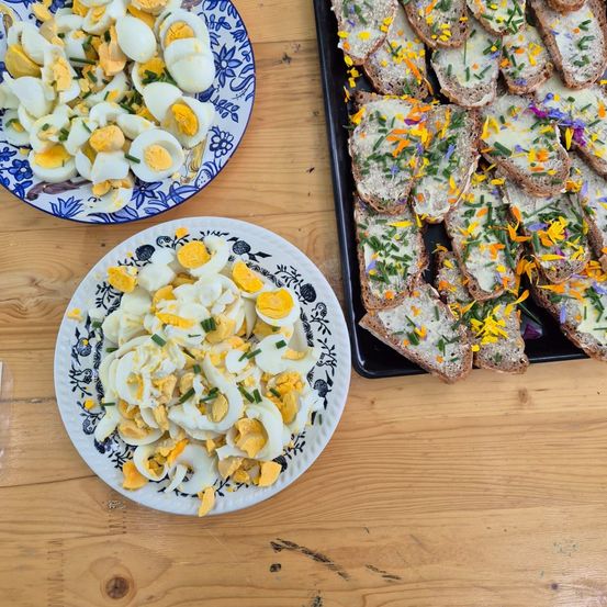 Zwei Teller mit pochierten Eiern und Brot, die mit Käse und Blumen belegt sind, stehen auf einem Holztisch.