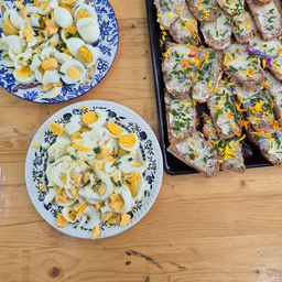 Zwei Teller mit pochierten Eiern und Brot, die mit Käse und Blumen belegt sind, stehen auf einem Holztisch.