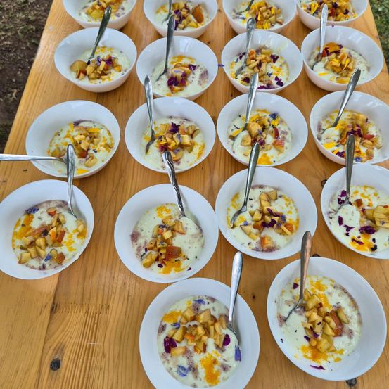 Ein Tisch mit mehreren Schüsseln mit Pfirsich-Creme-Dessert, gekrönt von Blütenblättern. Jede Schüssel hat einen silbernen Löffel.