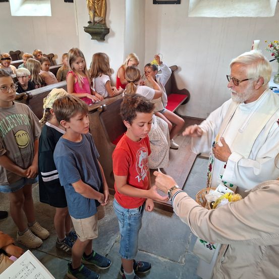 Ein Priester reicht einem jungen Jungen während einer religiösen Zeremonie in einer Kirche eine Kerze, wobei Kinder zuschauen.