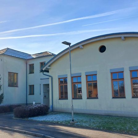 Ein modernes Gebäude mit einem gebogenen Dach und mehreren Glasfenstern. Es gibt Sträucher und Schnee auf dem Boden.