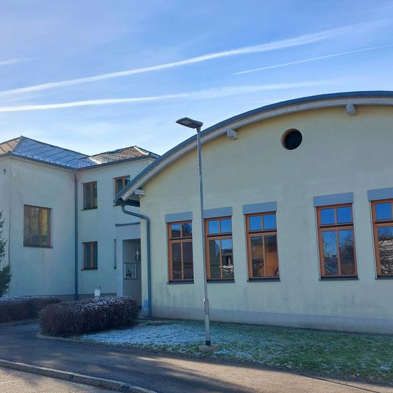 Ein modernes Gebäude mit einem gebogenen Dach und mehreren Glasfenstern. Es gibt Sträucher und Schnee auf dem Boden.