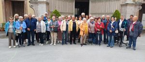 Eine Gruppe älterer Menschen posiert für ein Foto vor einem prunkvollen Gebäude. Einige tragen Brillen und halten Stöcke.