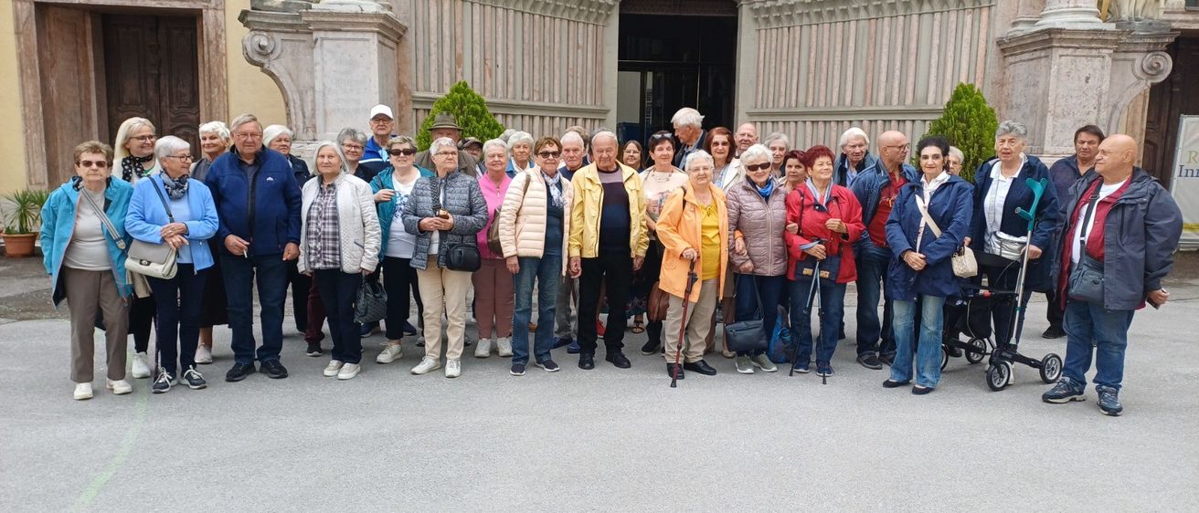 Eine Gruppe älterer Menschen posiert für ein Foto vor einem prunkvollen Gebäude. Einige tragen Brillen und halten Stöcke.