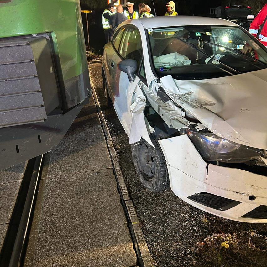 A white car is wrecked and stuck on the side of the road next to a green train at night.