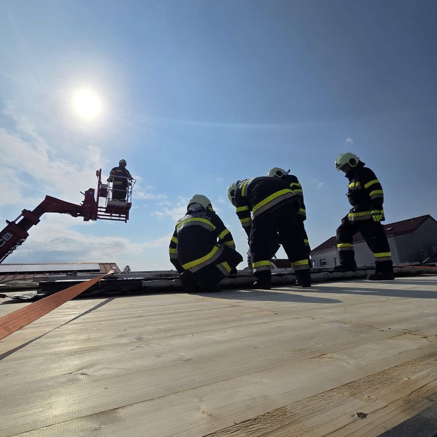 Eine Gruppe von Feuerwehrleuten arbeitet auf einem Dach mit Solarpanelen. Einer ist in einer Hubarbeitsbühne, während andere auf dem Dach sind.