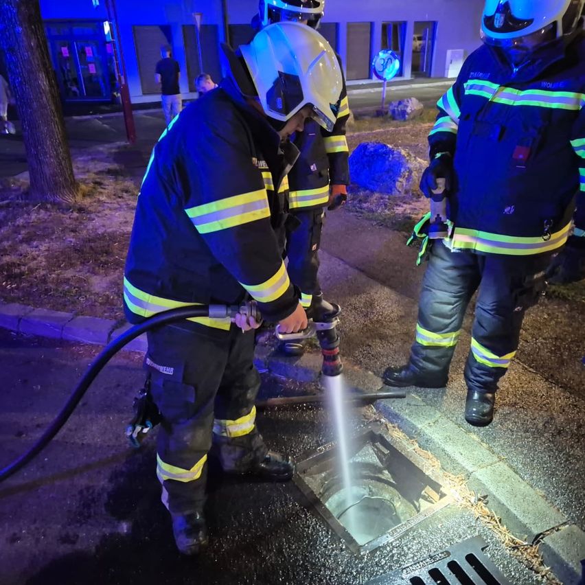 Firefighters are cleaning a sewer grate with a high-pressure water sprayer.