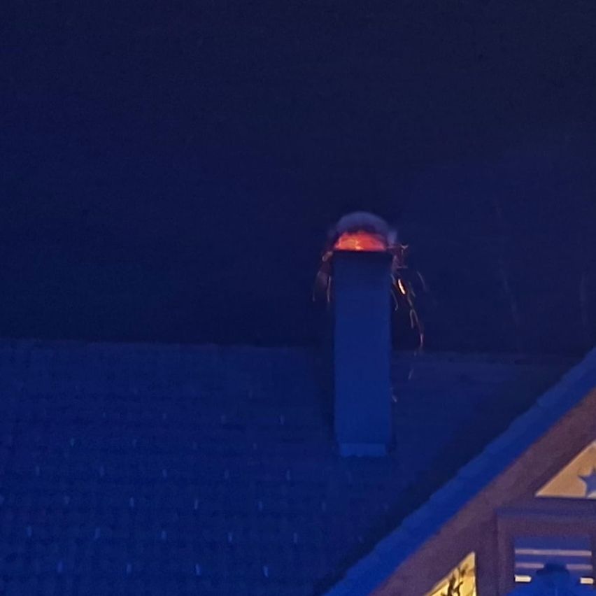 Eine Nachtansicht eines Hauses mit einem Schornstein auf dem Dach. Der Schornstein hat ein Feuer mit einem hellen Leuchten. Das Haus hat ein sternförmiges Fenster.