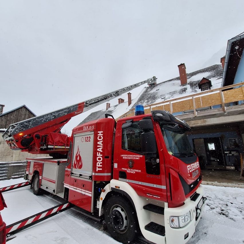 Ein roter Feuerwehrwagen mit ausgefahrener Leiter steht vor einem Gebäude bei schneebedecktem Wetter.