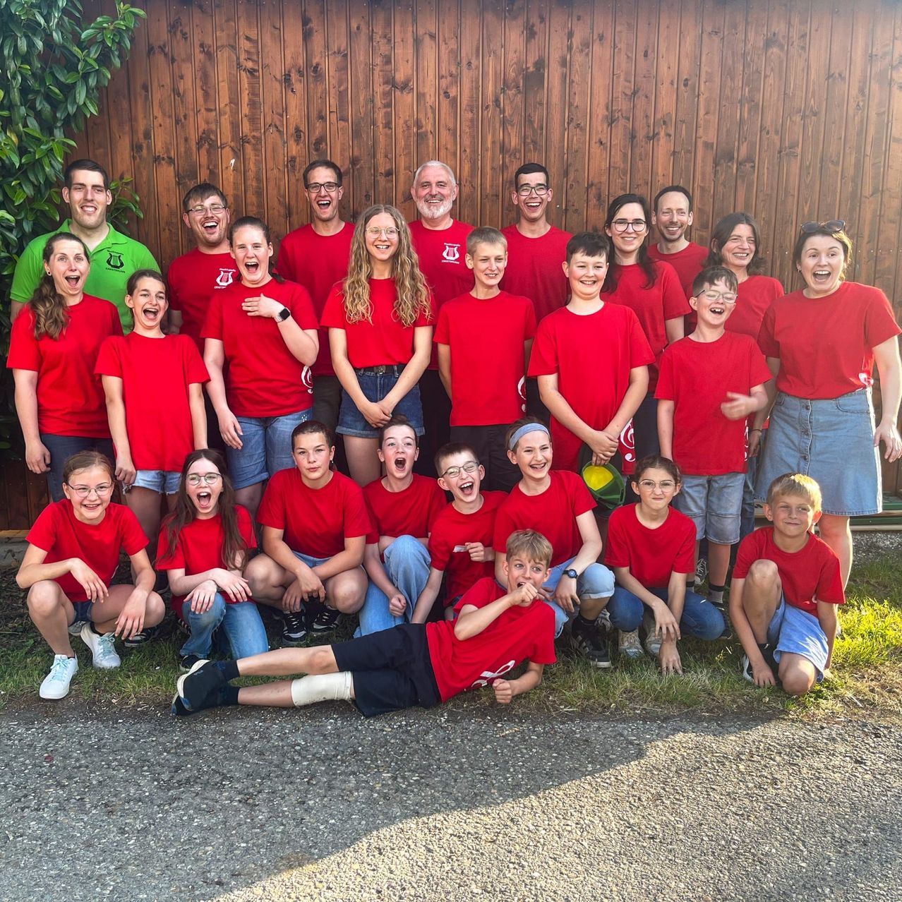 Eine Gruppe von Menschen in roten Shirts, einige mit Brille, posiert für ein Foto vor einer Holzwand.