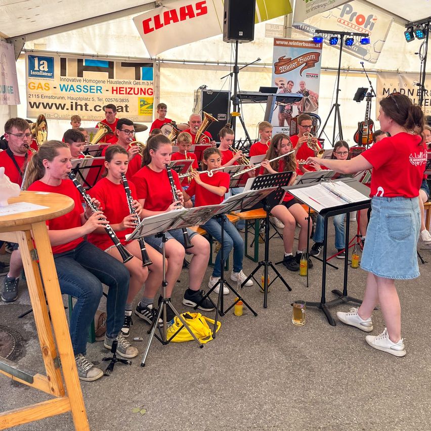 Eine Band probet in einem Zelt mit Musikinstrumenten. Eine Frau in einem roten Shirt dirigiert sie.