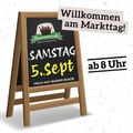 Ein Holzschild mit einer Tafel, die einen Markttag am Samstag, 5. September, ab 8 Uhr ankündigt. Das Schild zeigt ein Logo und Text auf Deutsch.