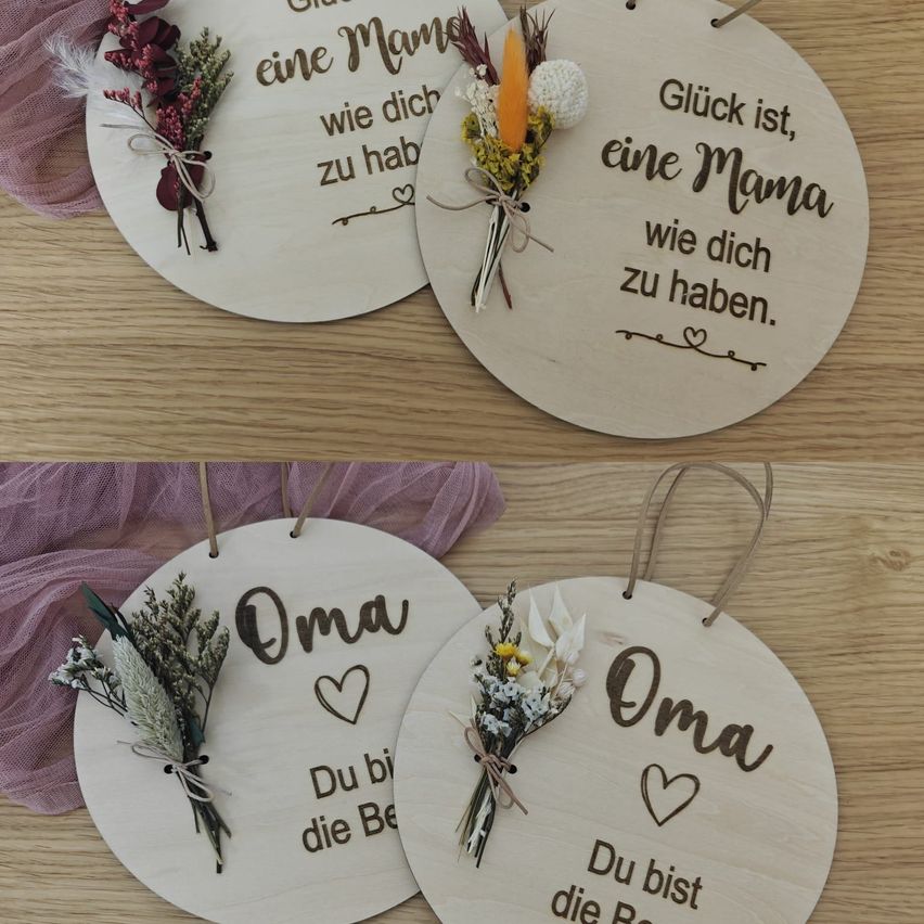 Drei runde Holzornamente mit Blumen und Text, eines sagt 'Oma' und die anderen beiden 'Glück ist, eine Mama wie dich zu haben'. Alle Ornamente haben oben eine Blumenarrangement.