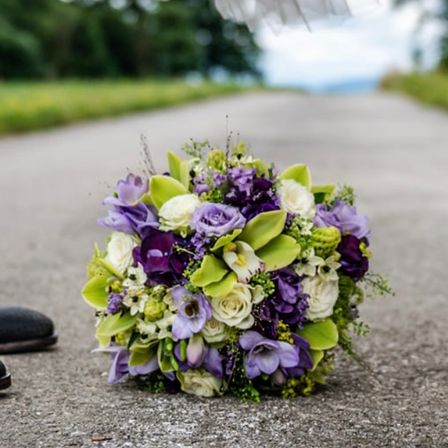 Ein schöner Brautstrauß mit lila und weißen Blumen liegt auf einem Kiesweg, mit einem Brautschuh in der Nähe.