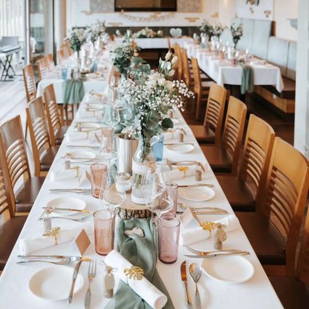 Ein langer Tisch mit Tellern, Weingläsern, Besteck und Blumen für eine besondere Veranstaltung.