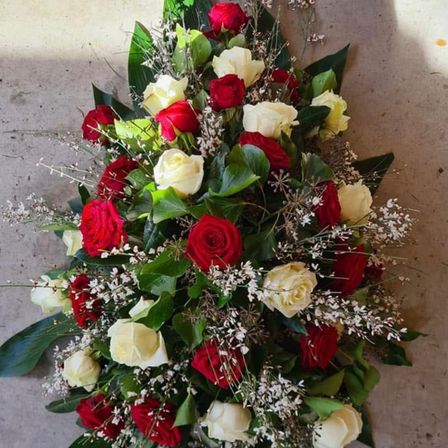 Ein großes Blumenarrangement mit roten und weißen Rosen, verziert mit grünen Blättern und kleinen weißen Blüten, auf einer Betonfläche platziert.