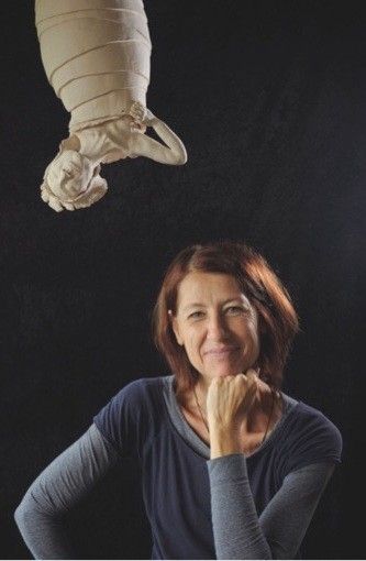 A woman poses for a photo with a white sculpture of a woman floating above her head.