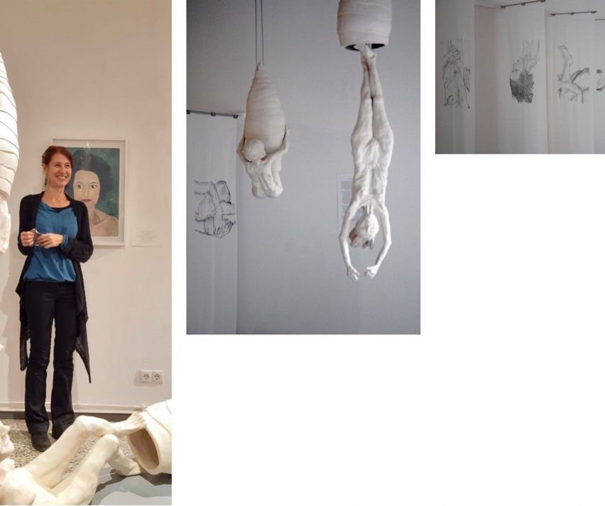 An art exhibit displays sculptures, one person standing and smiling, and a drawing of a woman's body.