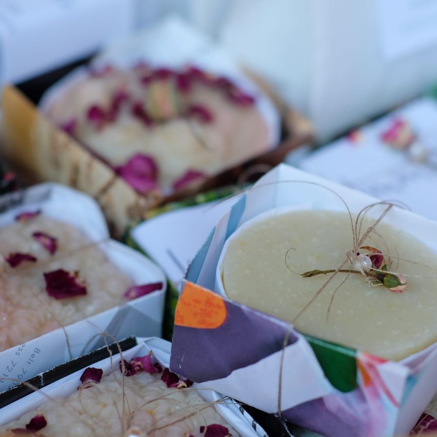 Mehrere Seifen in dekorativen Schachteln mit Blütenblättern obenauf, auf einem Tisch angeordnet, mit einigen verschwommenen im Hintergrund.