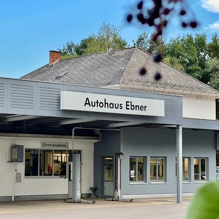 Das Äußere eines Volkswagen-Servicecenters mit einem Schild, das 'Autohaus Ebner' lautet. Ein Auto ist draußen geparkt.